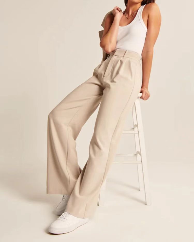 High-waist pleated wide-leg pants in beige, styled seated on a stool