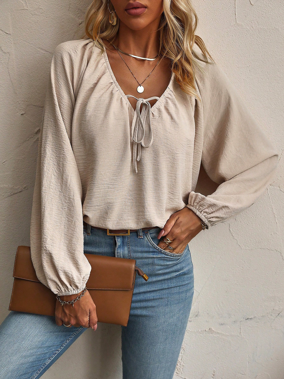 Beige tie-neck blouse with balloon sleeves, front view with a brown clutch